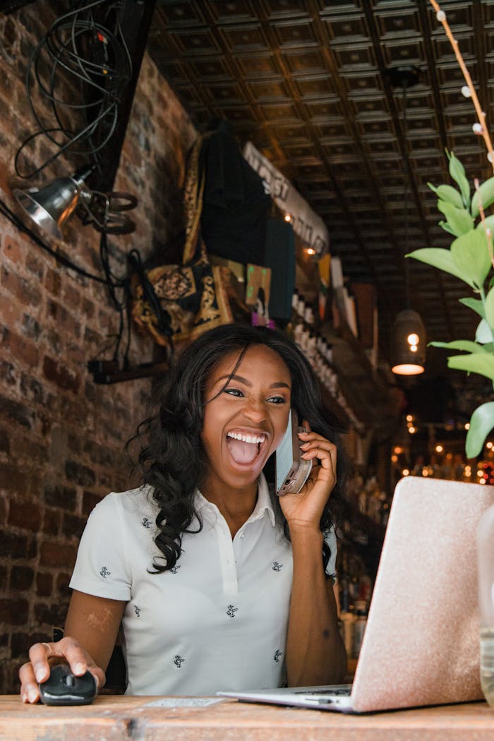 Excited small business owner laughing while talking on phone in a cozy bar setting.